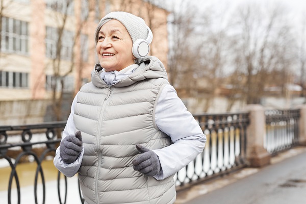 Waist up portrait of active senior woman running outdoors in winter and smiling happily
