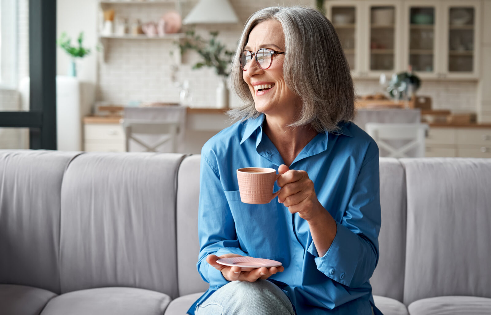 Older woman sitting on sofa enjoying a cup of tea.
